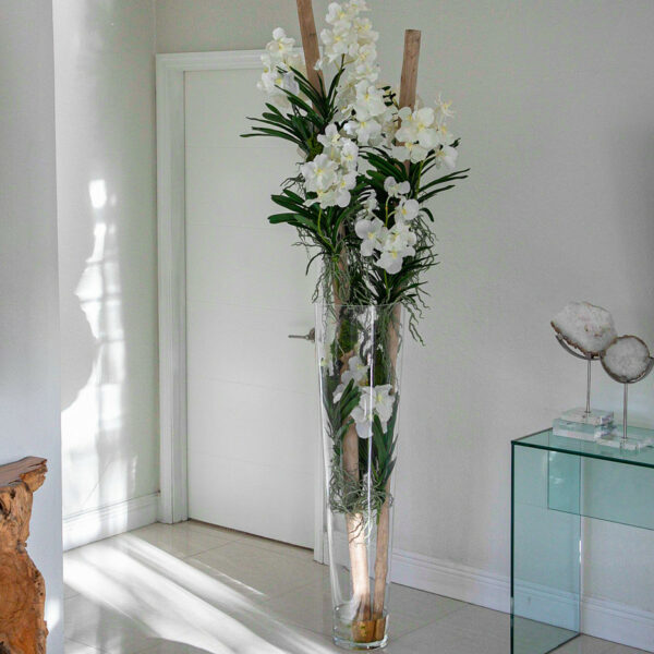 White Vanda orchids and floating wood inside a large conical glass vase.